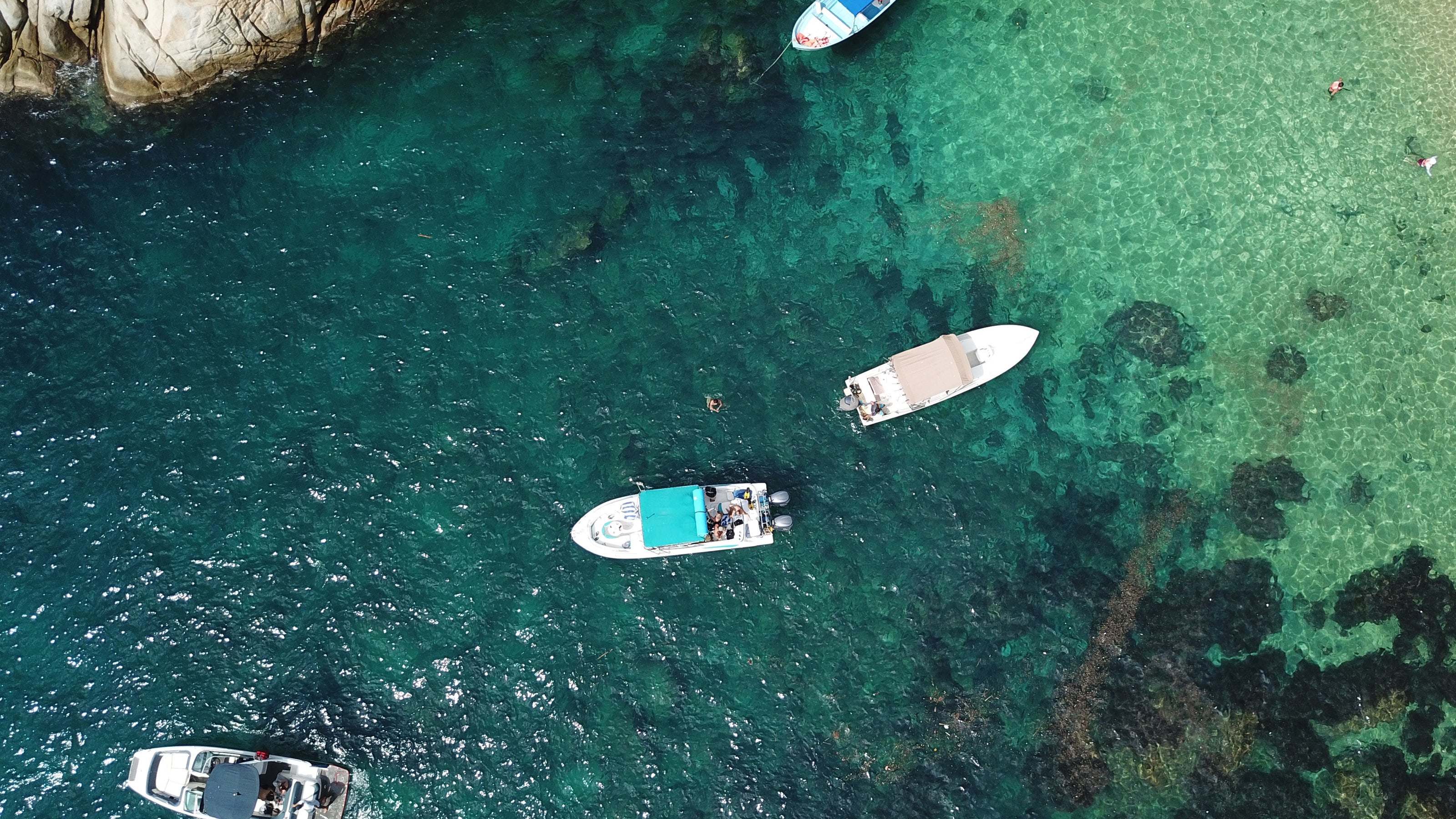Una cala vista desde arriba: agua profunda, arrecife, arena y una lancha anclada.