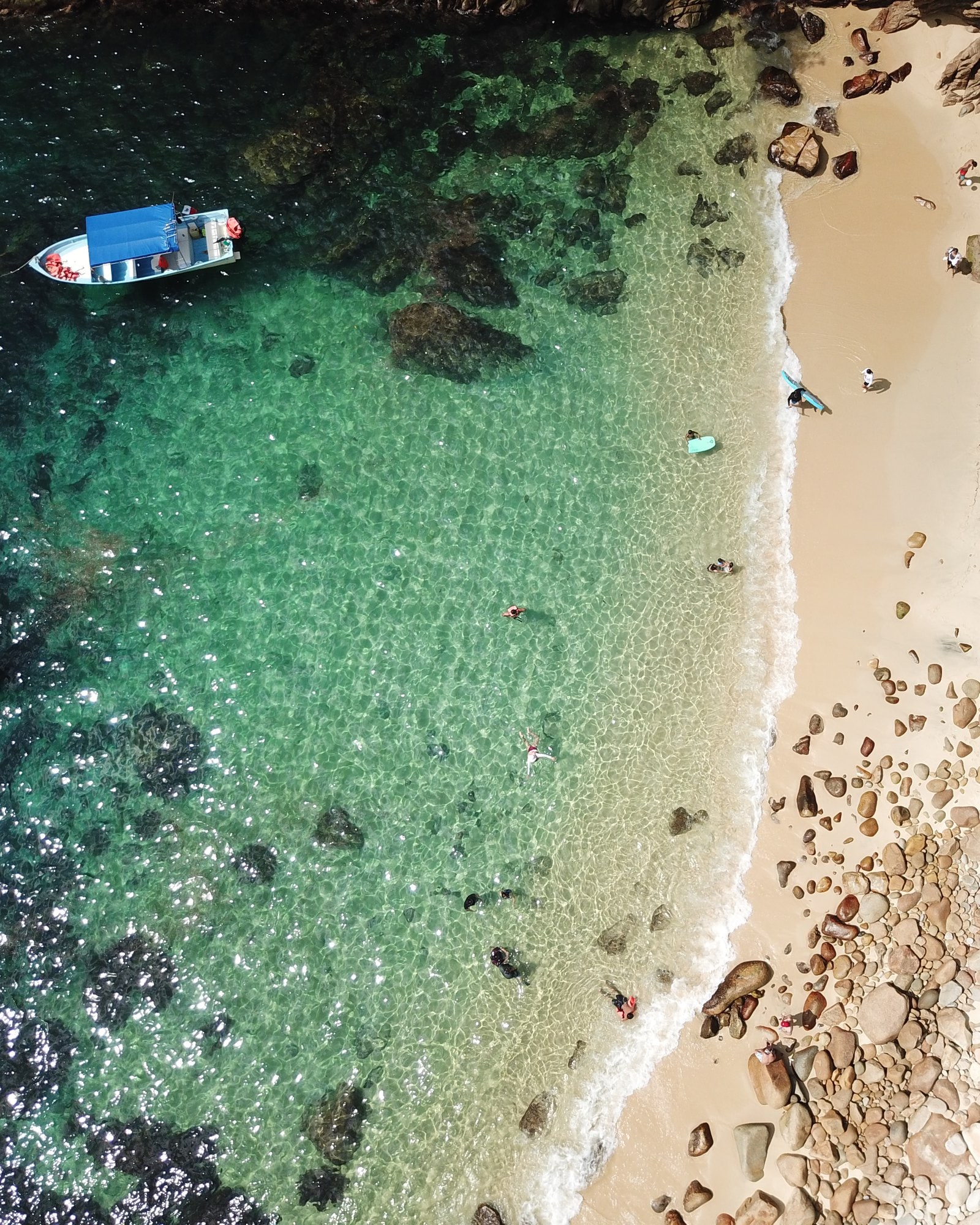 Una cala vista desde arriba: agua profunda, arrecife, arena y una lancha anclada.